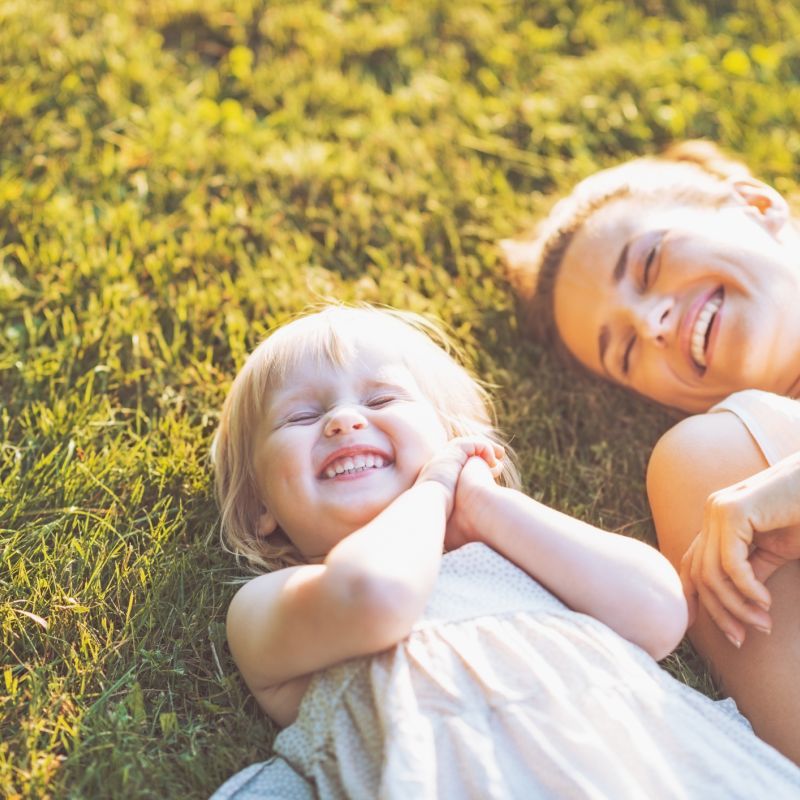 Smiling Mother and Baby Laying in Meadow